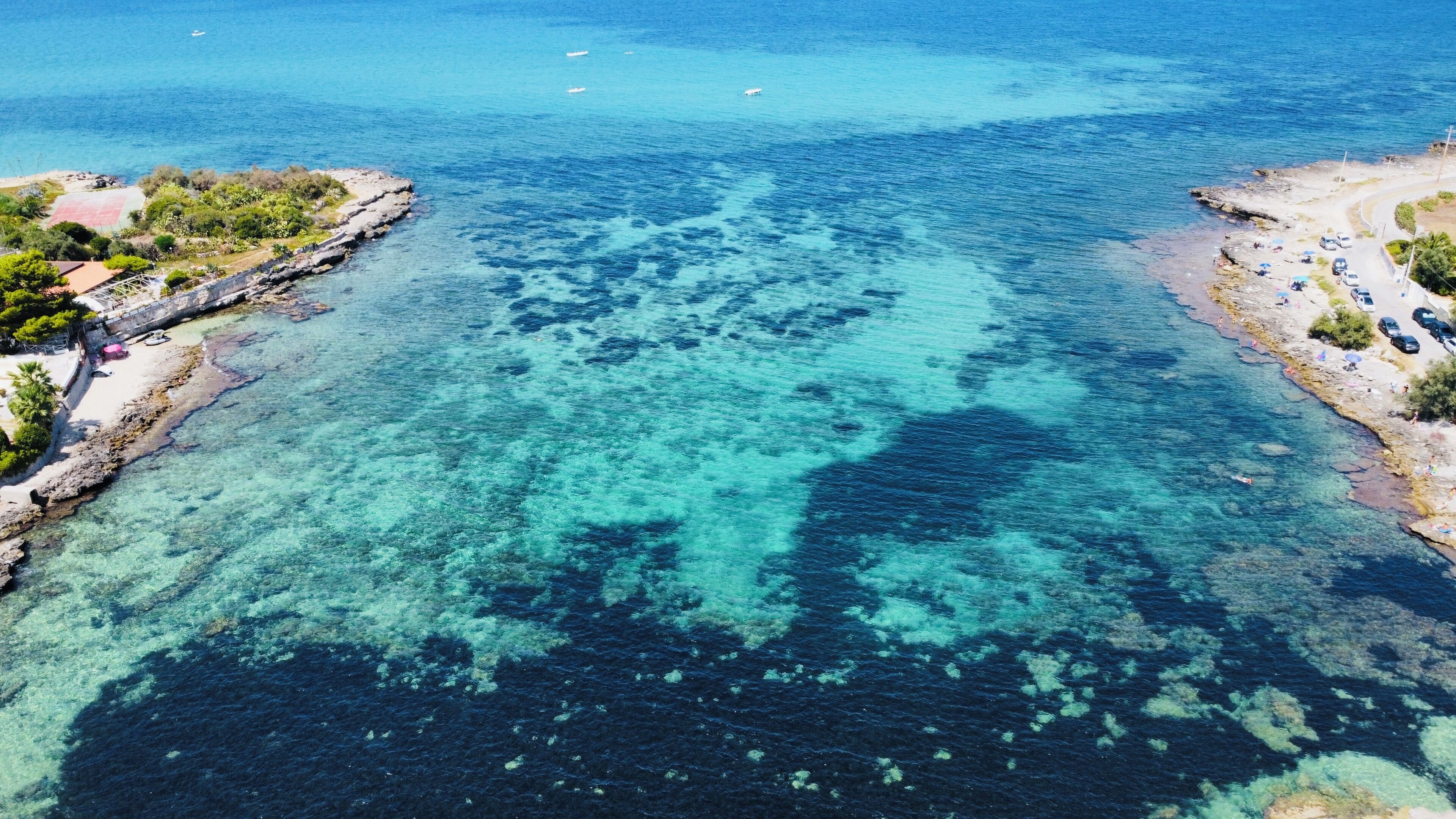 Una zona costiera con acque limpide, rocce e un percorso lastricato lungo la spiaggia.