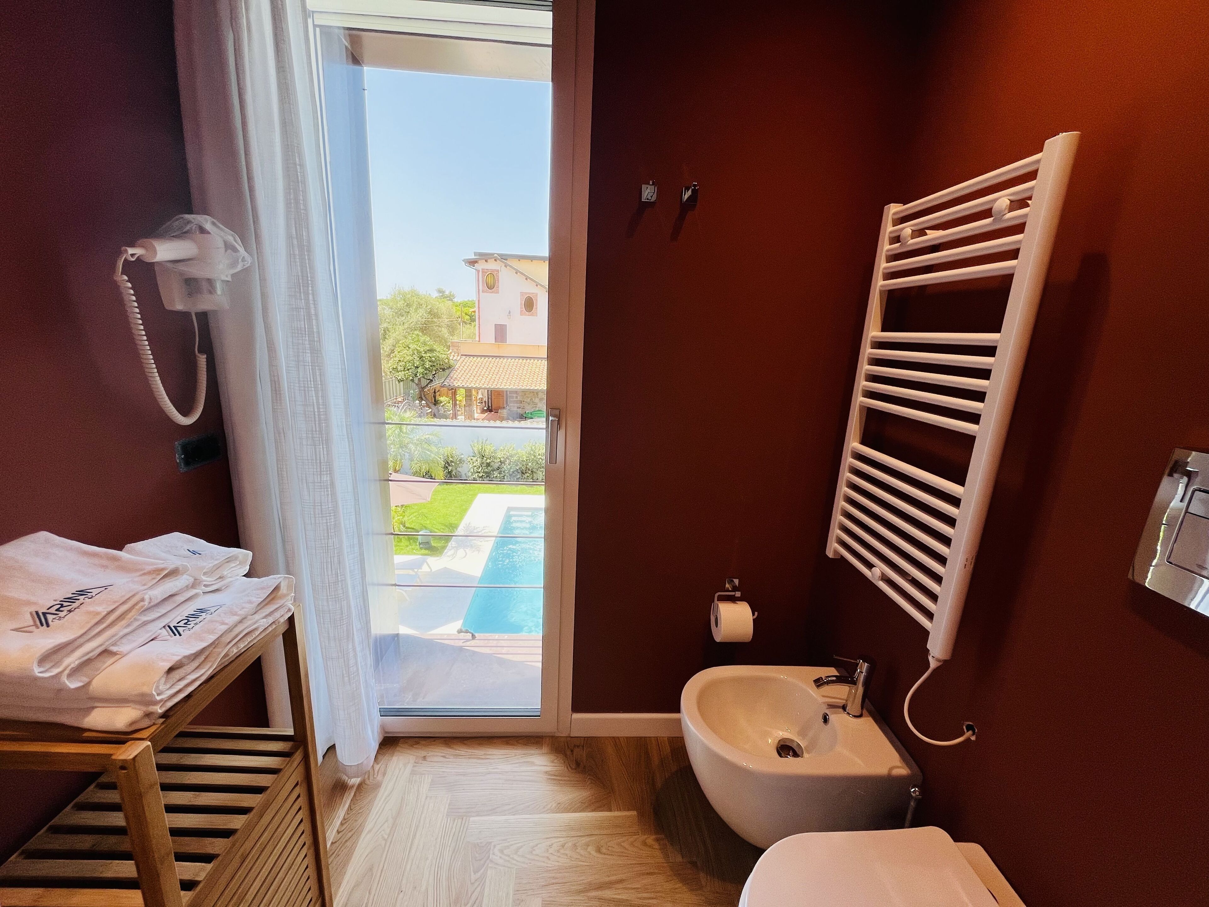 Un baño con suelo de madera, un lavabo, un perchero y vistas a una piscina y una casa.