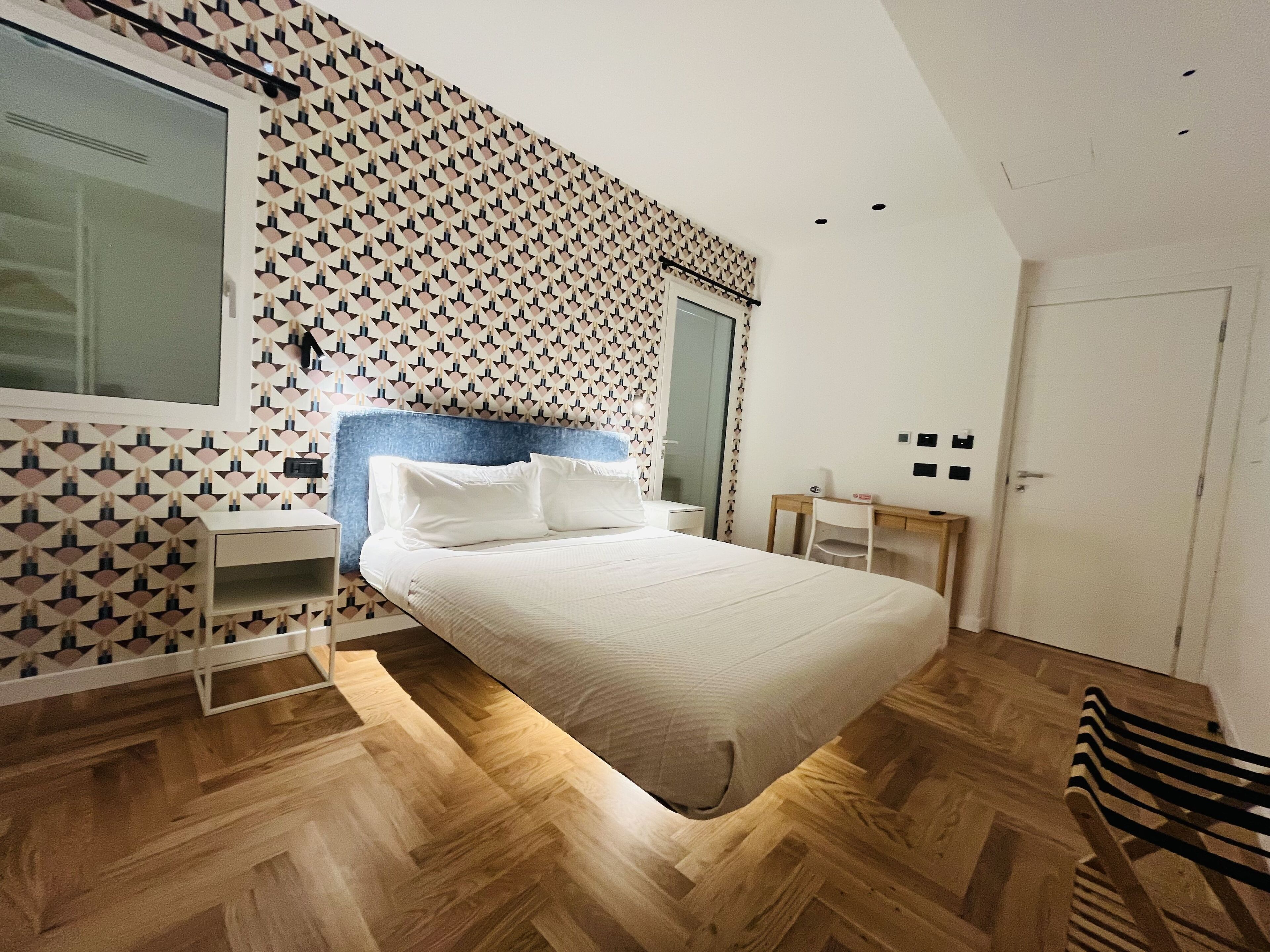 Un dormitorio moderno con pared de diseño geométrico, una cama grande, un escritorio y una silla.