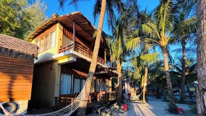 Un bungalow situé en bord de mer, doté d’un toit de chaume, de balcons en bois et d’un hamac.