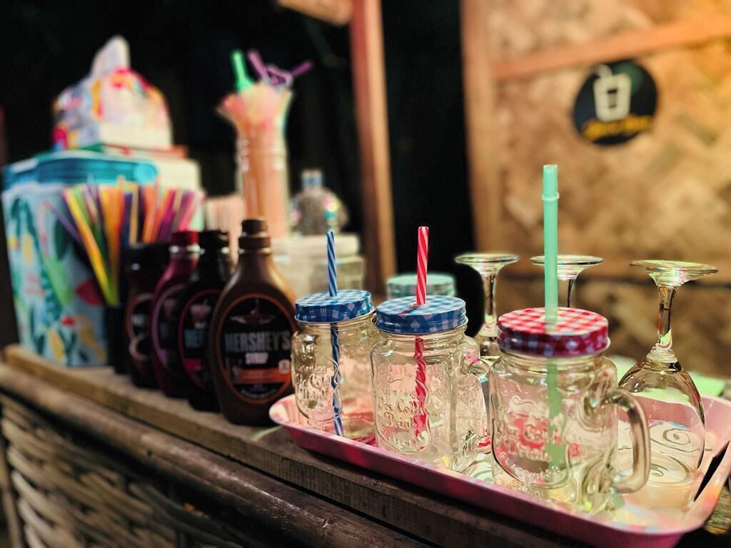 A tray with various jars and glasses, some with lids and straws, on a wooden surface.