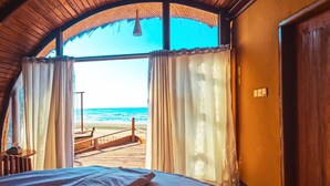 Une pièce dotée d’un plafond en bois, d’un plafond cintré et d’une grande fenêtre avec des rideaux, donnant sur une plage.