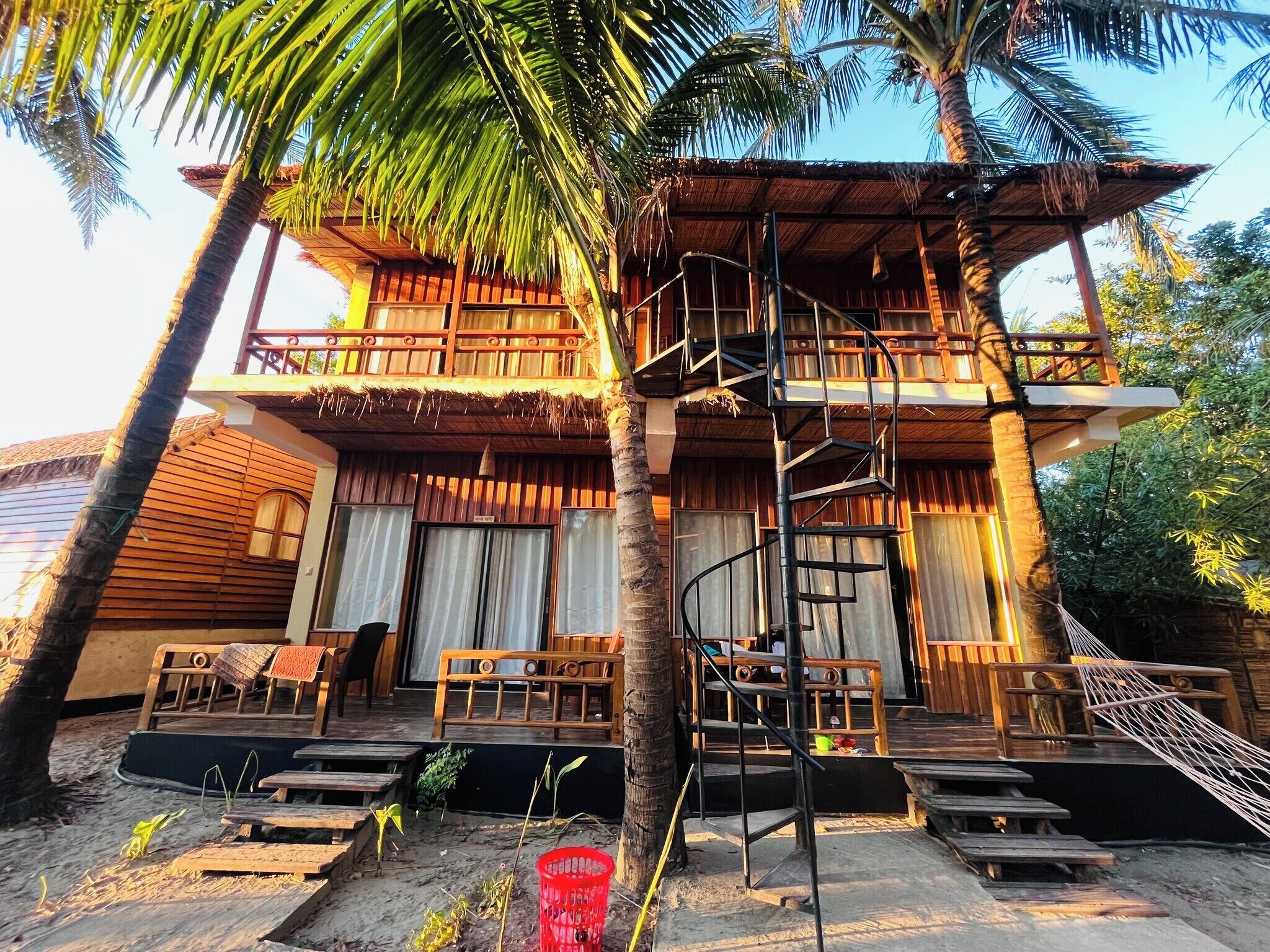A two-story wooden building with a spiral staircase, outdoor seating, and a thatched roof.
