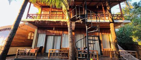A two-story wooden building with a spiral staircase, outdoor seating, and a thatched roof.