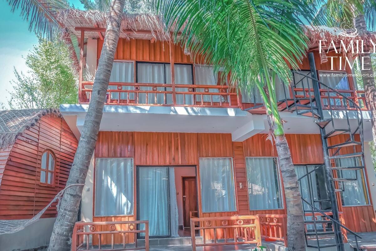 Una casa de madera de dos pisos con balcón, ventanas amplias y una escalera.