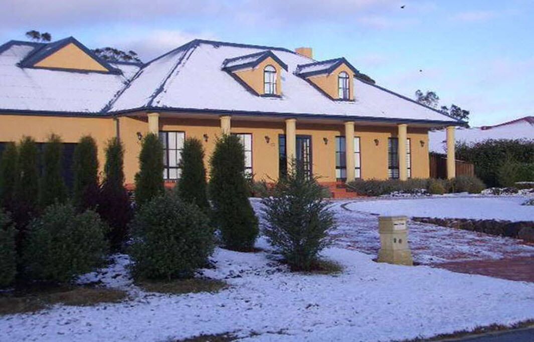 A two-story house with a snow-covered roof and a yellow facade.