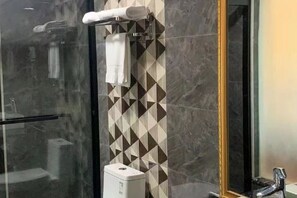 A bathroom with a glass shower enclosure, a towel rack with a white towel, a wall with a geometric pattern, and a mirror with a gold frame. - Qiongzhong Runfeng Business Hotel (Qiongzhong)