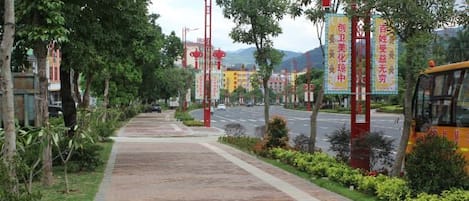 A paved walkway lined with trees and red poles with banners.