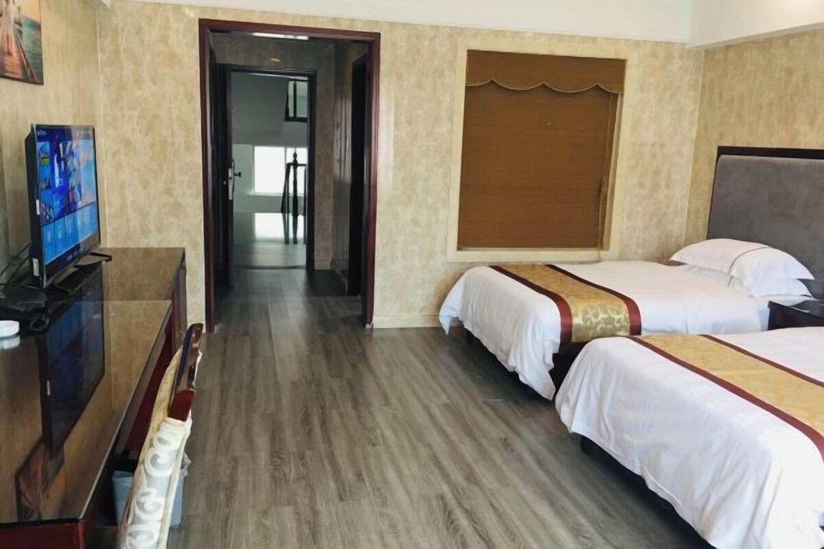 A hotel room with two beds, a TV, and a wooden floor.