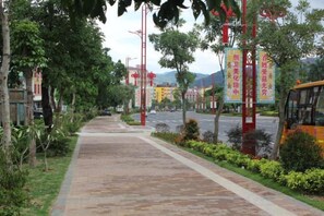 Un sendero pavimentado bordeado de árboles y arbustos, un poste rojo con un letrero y un autobús amarillo al fondo.