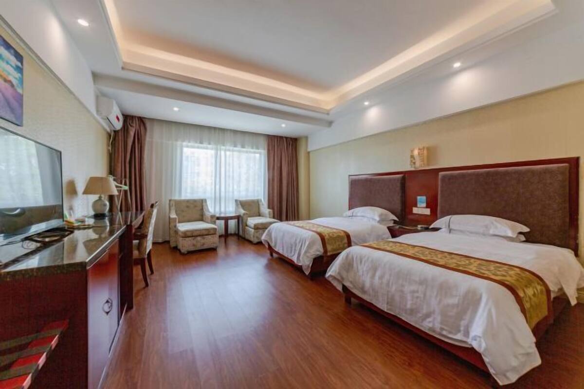 Une chambre d’hôtel avec deux lits, un bureau, une chaise, une télévision et une fenêtre avec des rideaux.