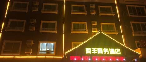 A hotel with multiple floors, air conditioning units, and a brightly lit entrance.