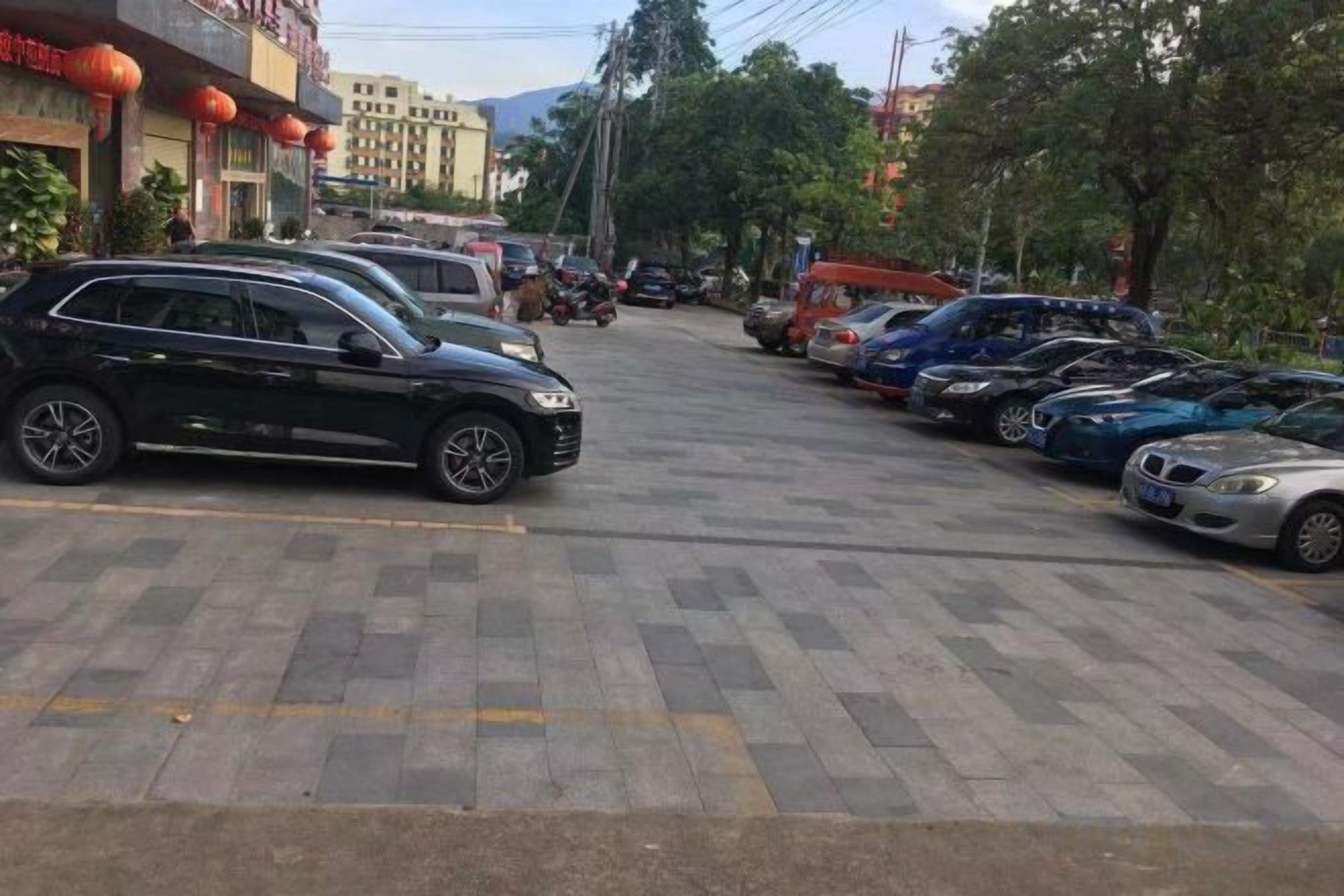 Ein Parkplatz mit mehreren parkenden Autos, ein Gebäude mit roten Laternen und Bäume im Hintergrund.
