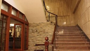 A staircase with wooden steps and a metal railing, leading to a room with a stone wall and a wooden door.