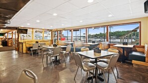Un restaurante espacioso con grandes ventanales que ofrecen vistas al frente marítimo. Mesas y sillas dispuestas para comer.