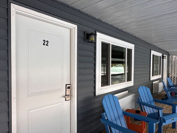 Una hilera de sillas Adirondack azules frente a un edificio con una puerta blanca que dice '22'.