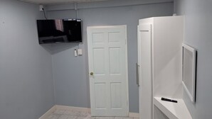 A room with a white door, a mounted TV, and a white cabinet with a remote control on top. - Breadfruit Lodge Bago 
 (SCARBOROUGH)