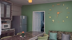 A kitchen with a marble countertop, green chairs, a patterned sofa, and a wall clock. - Breadfruit Lodge Bago 
 (SCARBOROUGH)