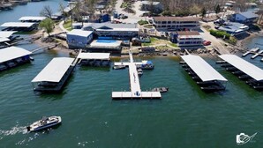 Eine Vogelperspektive auf einen Yachthafen mit vertäuten Booten, einer zentralen Pier und Gebäuden mit flachen Dächern.