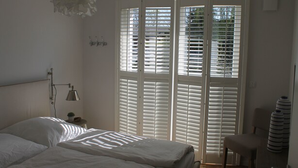 A bedroom with a bed, a nightstand, a lamp, and a window with blinds. - Premium vacation apartment Alter Sandweg incl. beach chair  (Scharbeutz)