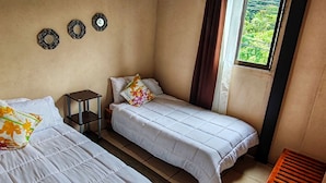 A room with two beds, a small table, and a window with a view of greenery. - Hostel Coati Place Bed & Breakfast  (Monteverde)