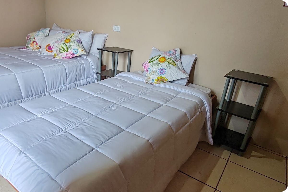 Dos camas con ropa de cama a juego y almohadas coloridas, dos mesitas de noche y un suelo de baldosas.