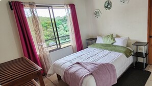 A bedroom with a bed, bedside tables, a window with curtains, a wooden door, and a small table. - Hostel Coati Place Bed & Breakfast  (Monteverde)