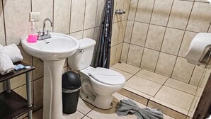 A bathroom with a sink, toilet, and a small table with towels and a trash bin. - Hostel Coati Place Bed & Breakfast  (Monteverde)