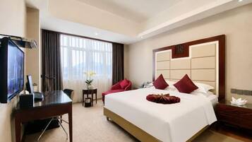 A hotel room with a large bed, a desk, a TV, and a window with curtains.