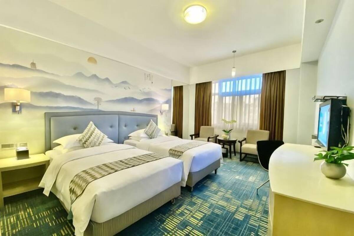 Une chambre d’hôtel avec deux lits, un bureau, une chaise, une télévision et une grande fenêtre avec des rideaux.
