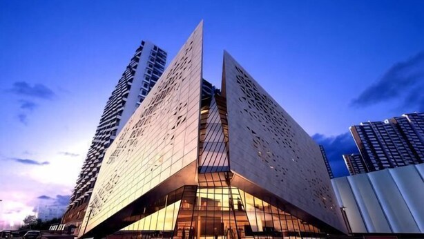 A modern building with a unique angular design, featuring large glass windows and a prominent entrance. - Overseas Chinese Hotel (Nan'an)