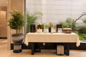 A reception area with a table displaying various items, a potted plant, and a view of greenery outside.