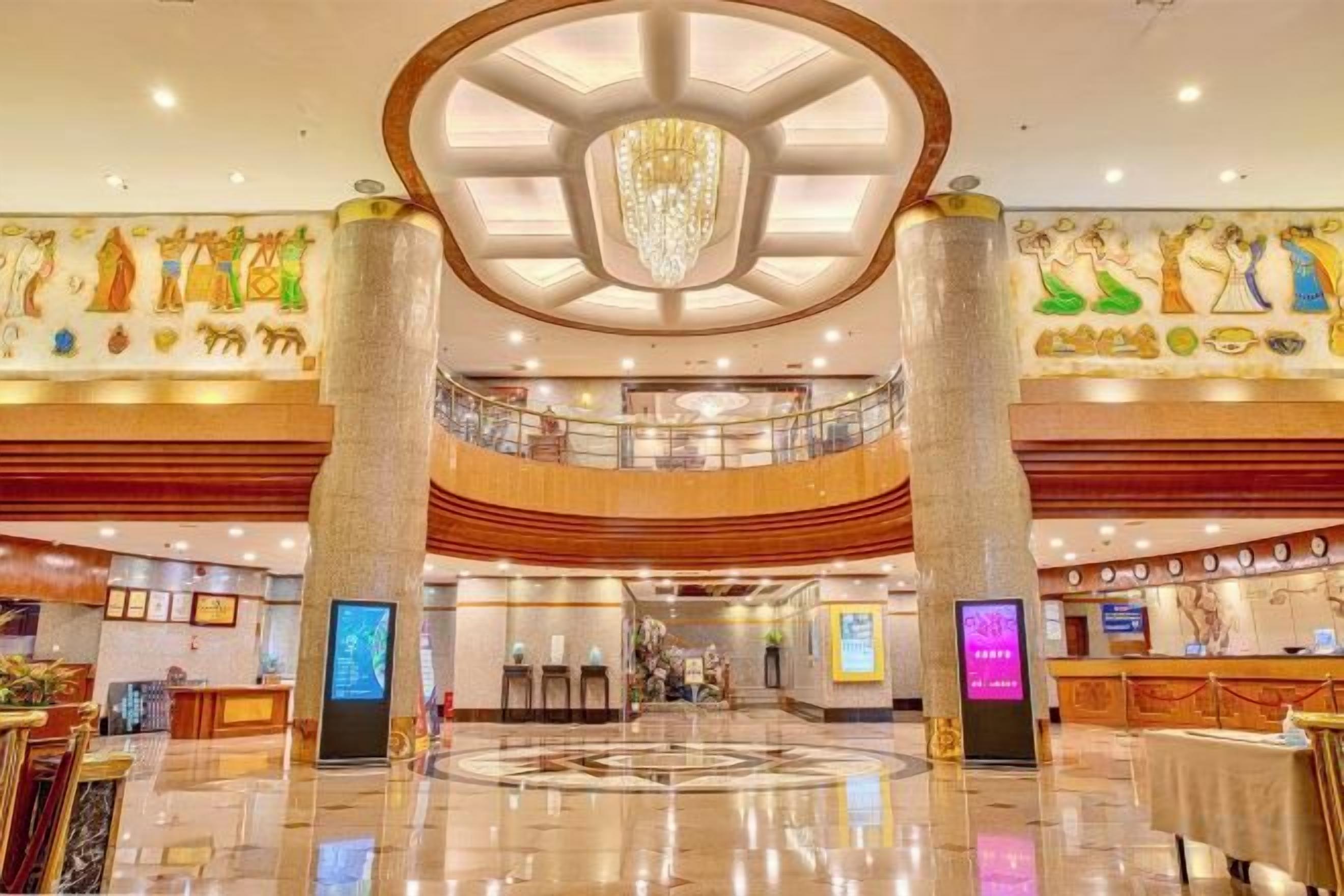 A hotel lobby with a central chandelier, a reception desk, and a circular floor design.