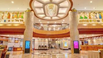 A hotel lobby with a central chandelier, a reception desk, and a circular floor design.