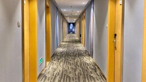 A hotel corridor with patterned carpet, wooden doors, and a blue carpeted area at the end. - Overseas Chinese Hotel (Nan'an)