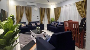 A living room with two sofas, a coffee table, and a TV. There are curtains, a clock, and a ceiling fan. - 3 Bed Flat - Sleeps 6 - Parking - Wifi (Adentan)