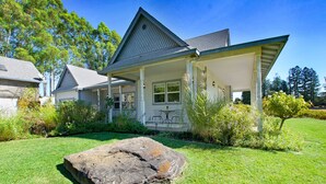 Ein Haus mit überdachter Veranda, einem Steinuntergrund und einem gepflegten Rasen mit einem großen Felsen im Vordergrund.
