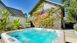 Ein Whirlpool in einem Garten mit einer von Efeu bewachsenen Steinmauer, einem Haus und üppiger Bepflanzung.