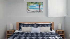 A bedroom with a bed, a nightstand, a white wardrobe, and a beach-themed painting on the wall. - Sunset Beach House - Remodeled - 1 block to beach (St. Catharines)
