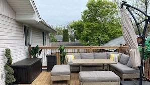 A wooden deck with a sectional sofa, two ottomans, and a small table. - Sunset Beach House - Remodeled - 1 block to beach (St. Catharines)