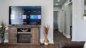 A modern living room with a flat-screen TV displaying various apps, a fireplace, and a decorative vase. - Sunset Beach House - Remodeled - 1 block to beach (St. Catharines)