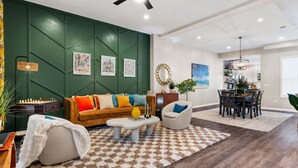 A modern living room with a green accent wall, a sofa set, a dining area, and a chandelier.