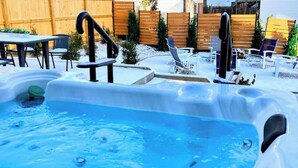 A backyard with a hot tub, wooden deck, and outdoor furniture.