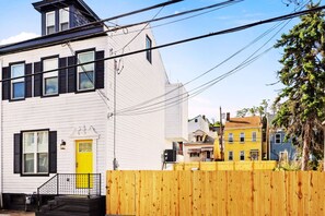 Un bâtiment blanc avec des volets noirs, une porte jaune et une clôture en bois à l’avant.