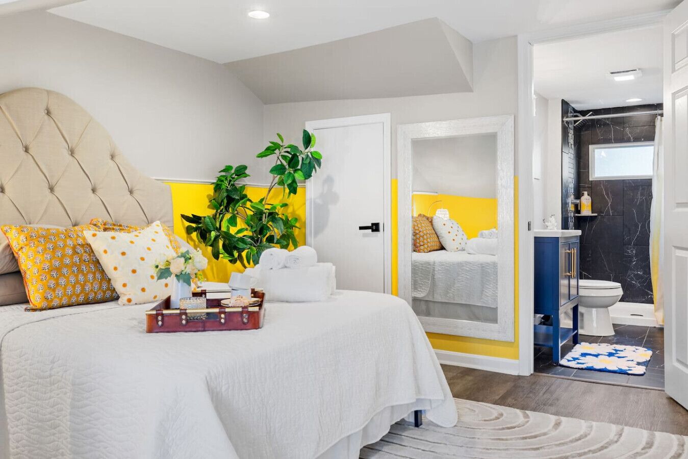 A modern bedroom with a large bed, a bedside table, a mirror, and a view into the bathroom.