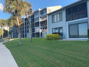 A multi-story residential building with balconies, a grassy lawn, and a pathway.