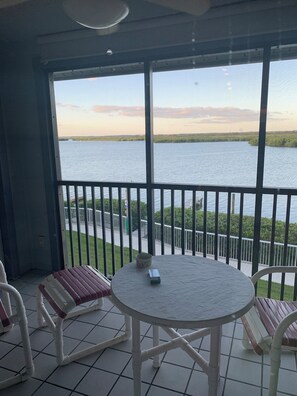 A balcony with a table and chairs, overlooking a body of water.