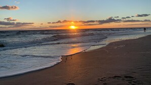 Una playa con olas, un atardecer y una persona caminando.