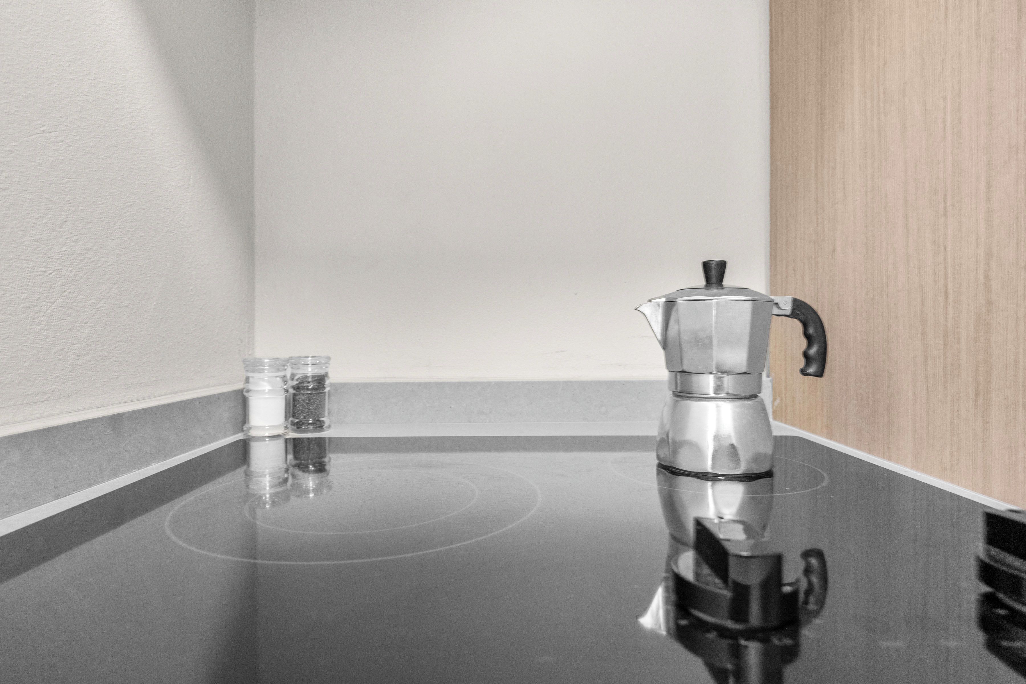 A kitchen with a black countertop, a stainless steel coffee maker, and two clear glasses.