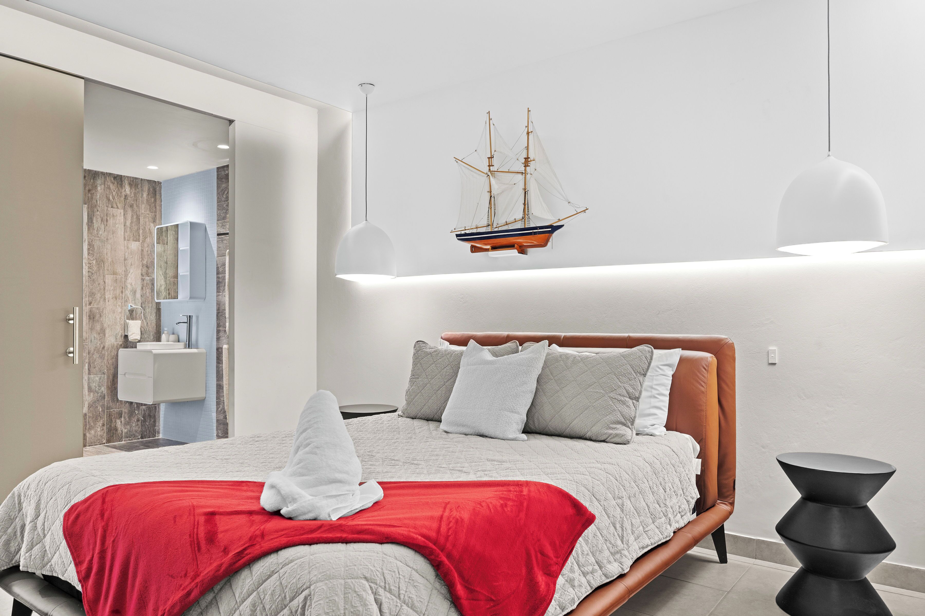 A modern bedroom with a wooden bed, a red throw blanket, and a ship model on the wall.
